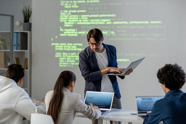 20230817125145 fpdl.in teacher with laptop standing by desk and bending over one of students while checking the task or consulting her at lesson 274679 9689 normal - Как выбрать компанию для внедрения и обслуживания программных продуктов 1С